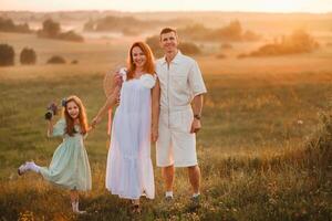 A beautiful happy family of three is standing in a field at sunset photo