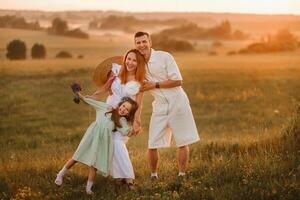 A beautiful happy family of three is standing in a field at sunset photo