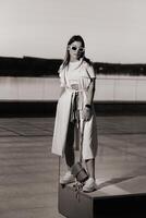 Stylish girl in glasses and a white summer coat in the city with a handbag photo