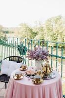 Delicate morning tea table setting with lilac flowers in Nesvizh castle, antique spoons and dishes on the table with a pink tablecloth photo