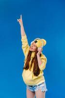 A pregnant girl in a yellow jacket and headphones stands on a blue background photo