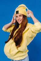 A pregnant girl in a yellow jacket and headphones stands on a blue background photo