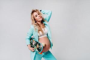 a pregnant girl in turquoise clothes with a skateboard in her hands on a gray background photo