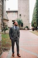A man with a beard in a strict grey three-piece suit with a tie in the old town of Sirmione, a Stylish man in a grey suit in Italy photo