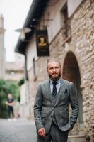 A man with a beard in a strict grey three-piece suit with a tie in the old town of Sirmione, a Stylish man in a grey suit in Italy photo