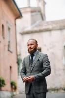 A man with a beard in a strict grey three-piece suit with a tie in the old town of Sirmione, a Stylish man in a grey suit in Italy photo