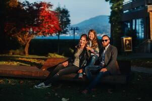 A happy family of three sits on a bench at a Sunny autumn sunset in Austria's Old town.A family poses in a small Austrian town against the backdrop of the Austrian Alps.Europe.Felden am see photo