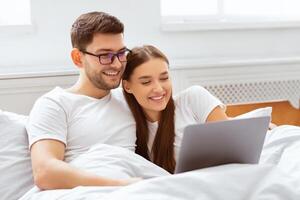 Weekend Leisure. Happy Spouses Using Laptop Watching Movie Sitting In Bed At Home. Selective Focus photo