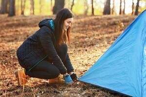 Happy adventurous girl setting camp in autumn forest, placing tent, empty space photo