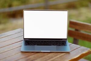 A sleek laptop sits on a rustic wooden table, surrounded by nature. The device has a blank screen, suggesting potential for creative work or relaxation outdoors. photo
