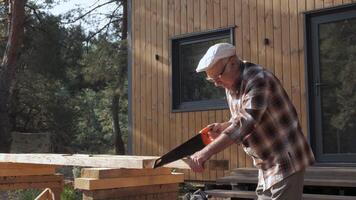 An experienced craftsman carefully saws a piece of timber for his rustic cabin, surrounded by trees. The sunlight filters through, creating a calm atmosphere. video