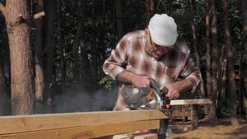 An experienced carpenter focuses intently while using a circular saw to cut timber outdoors. Sunlight filters through the trees, adding a serene atmosphere. video