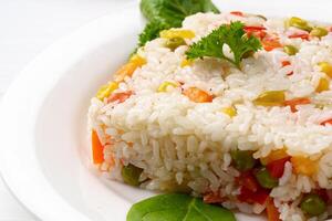 Cooked white rice mixed with colorful vegetables on white plate photo