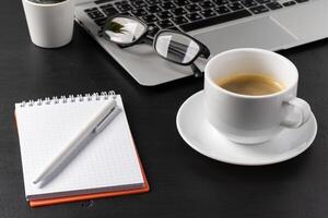 Notepad is on top of office desk table with laptop and supplies photo