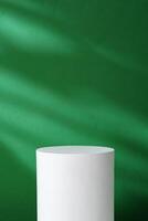 Plain white cylindrical pedestal against a green background with soft shadows in a bright interior setting photo