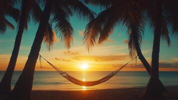 Serene sunset view over the ocean with a hammock strung between palm trees on a sandy beach photo