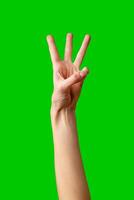 Human Hand Displaying the Number Three Against a Solid Green Background photo