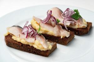 Open-faced sandwiches with herring and onions served on a white plate photo