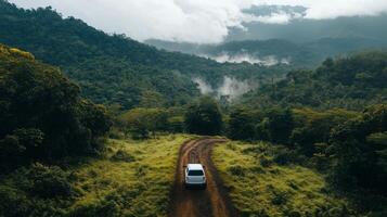A solitary vehicle travels along a winding dirt road through lush mountains and misty valleys on an overcast day in the countryside photo