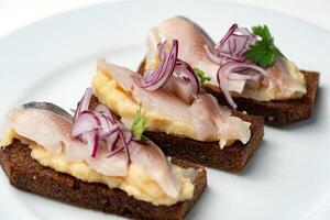 Open-faced sandwiches with herring and onions served on a white plate photo
