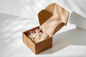 A simple brown gift box with natural filling sits elegantly on a light surface, capturing soft shadows photo