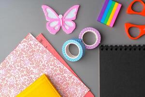 Crafting supplies arranged on a gray surface with a blank notebook, scissors, washi tape, and colorful embellishments photo