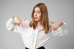 Young businesswoman standing against gray background and pointing her finger to copy space photo