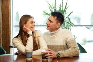 Smiling Couple Enjoying Warm Beverages at a Cozy Cafe on a Sunny Afternoon photo