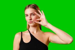 Young Woman Gesturing Silence With Finger on Lips Against Green Screen Background photo