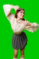 A young woman stands against a vibrant green screen, creating a finger frame with her hands as if visualizing a composition or focusing on a specific view. photo
