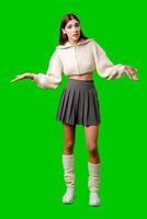 A woman is standing on a green screen backdrop, wearing a skirt and sweater. She appears poised and looking directly at the camera. photo