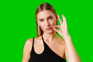Young Woman Gesturing Silence With Finger on Lips Against Green Screen Background photo