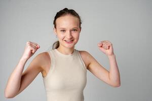 Young Woman in Casual Attire Smiling and Making a Fist Pump Gesture on a Plain Background photo