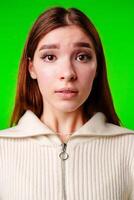 A woman wearing a white sweater stands in front of a vibrant green background. photo