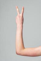 Raised Hand Making Peace Sign Against Plain Gray Background photo