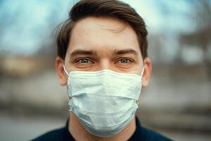 Portrait man in medical mask. Young man stands on light background and looking at camera. COVID-19 Pandemic Coronavirus. photo