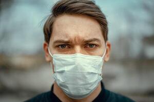 Portrait man in medical mask. Young man stands on light background and looking at camera. COVID-19 Pandemic Coronavirus. photo