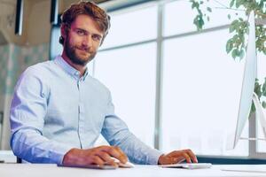 Young bearded businessman using his computer in a modern office place photo