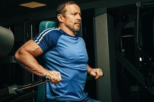 Senior man doing exercises for arms in a training machine in gym photo