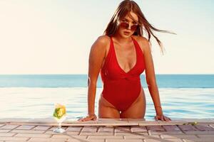 Tanned woman in red bikini in a pool with cocktail photo