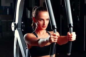 Young attractive woman doing exercises for arms in a training machine photo