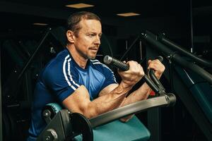 Senior man doing exercises for arms in a training machine in gym photo