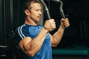 Senior man doing exercises for arms in a training machine in gym photo