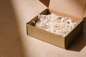 Open cardboard box with shredded paper packaging resting on a light brown surface illuminated by soft natural light photo