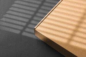 A cardboard box casting shadows on a dark surface in a striped light pattern photo