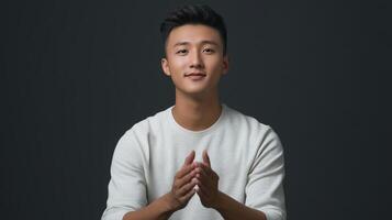 A young man smiles warmly while clapping his hands in a studio setting, showcasing a relaxed demeanor against a dark background photo