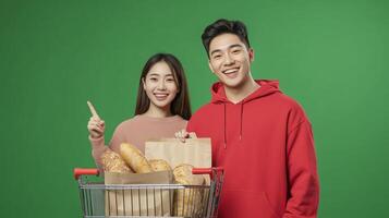 Young couple smiles while posing with fresh bread in a shopping cart against a green background in a bright indoor setting photo