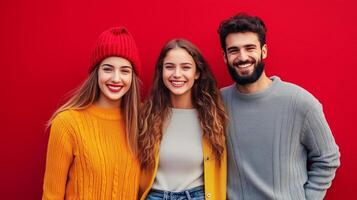 Three friends smiling together in front of a bright red wall during a sunny day in a casual urban setting photo