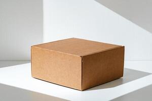 Simple brown cardboard box positioned on a white surface with soft angled shadows in natural light photo