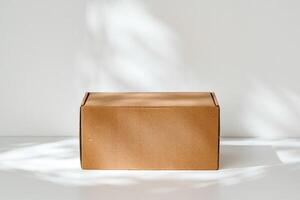 Simple brown cardboard box positioned on a white surface with soft angled shadows in natural light photo